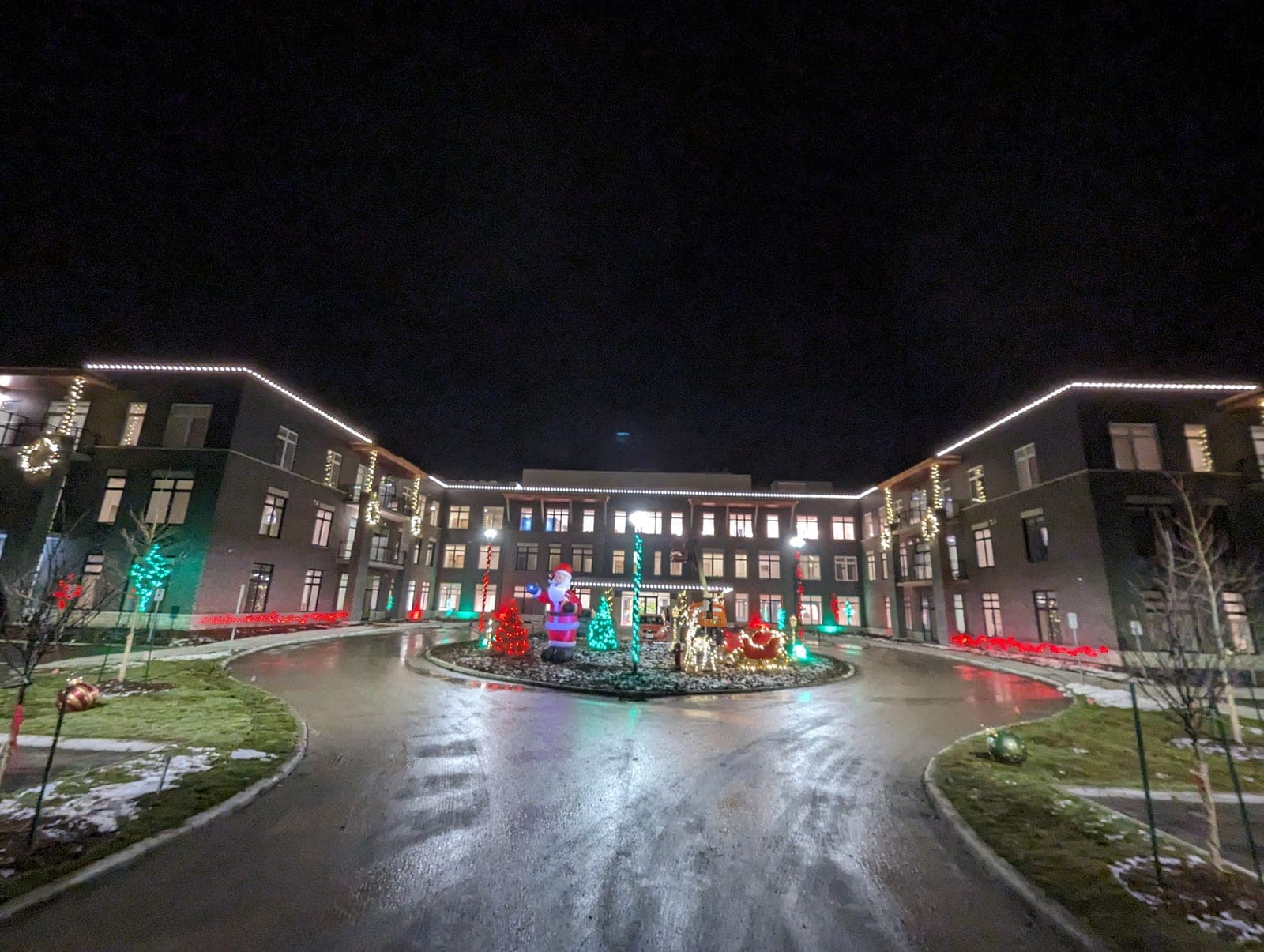 Commercial building entrance drive lit with warm-white roofline Christmas lights and a holiday display