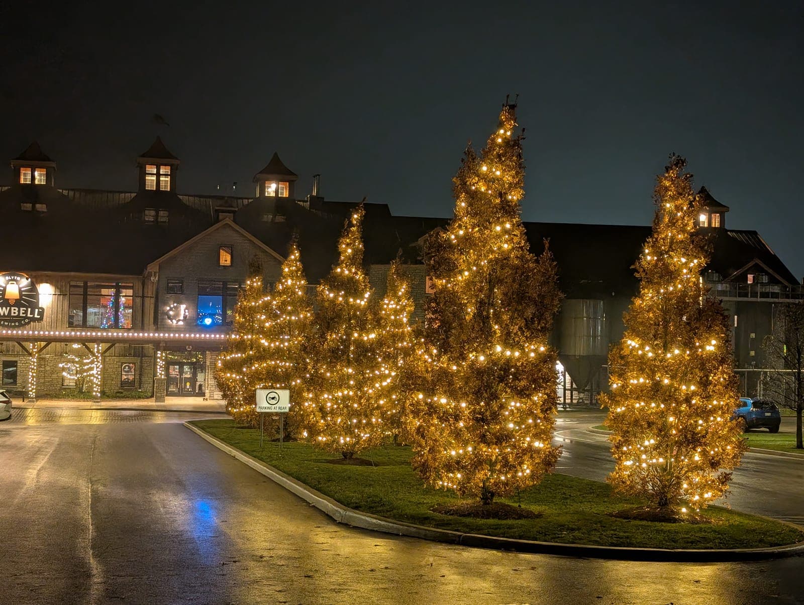 Warm-white wrapped trees lighting the entrance of a commercial brewery building at night