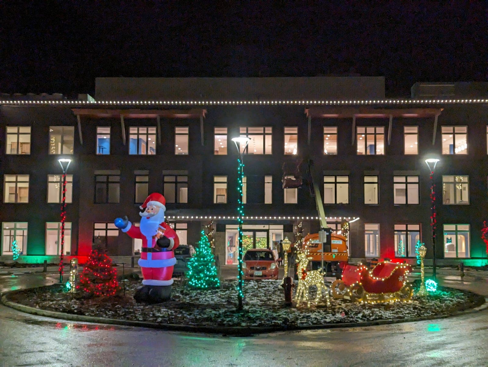Commercial building with warm-white roofline Christmas lights and a giant inflatable Santa, reindeer and sleigh display