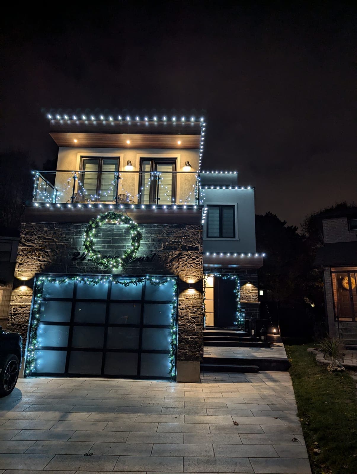 Modern two-storey home with cool-white roofline lights, a lit wreath and garland-framed glass garage