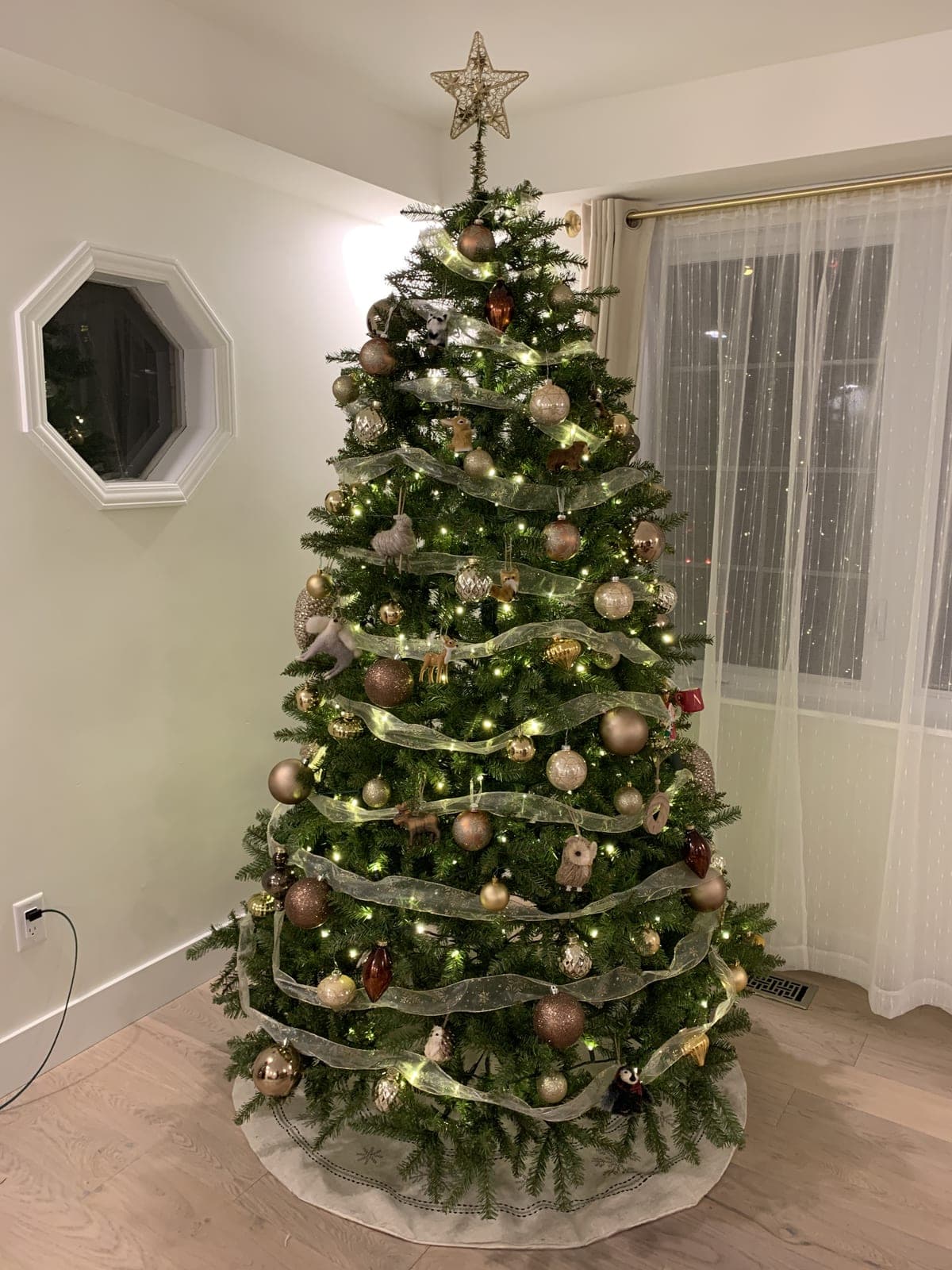 Decorated Christmas tree with warm-white lights and sheer ribbon garland in a bright corner