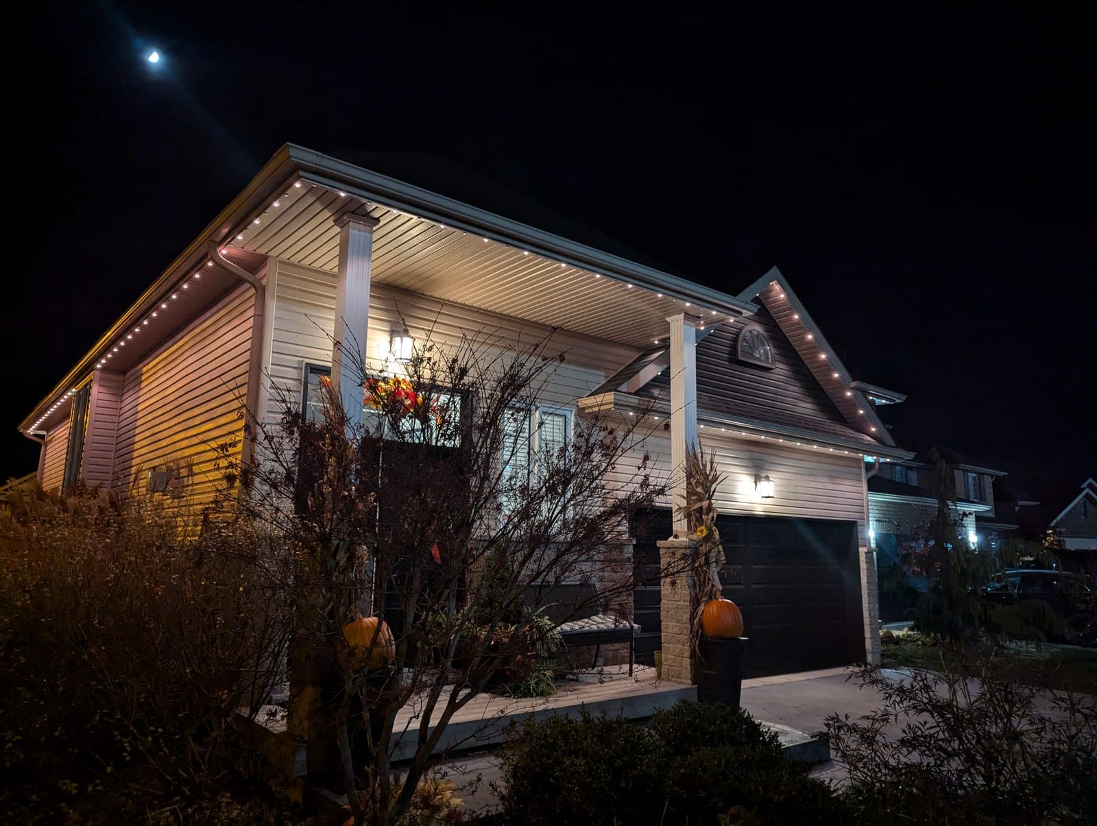 Home with warm-white eave lighting and autumn porch decor on a clear night
