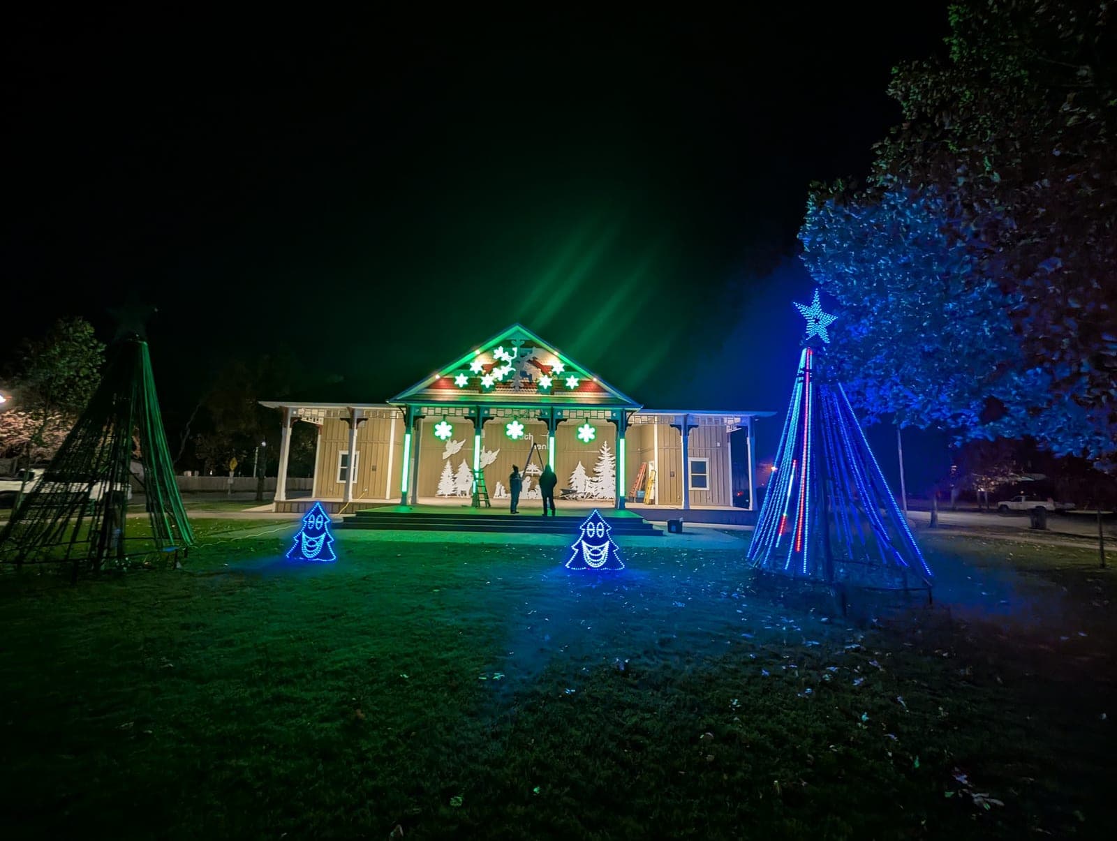 Animated LED Christmas light show illuminating a park pavilion with colour-changing tree frames and star displays.