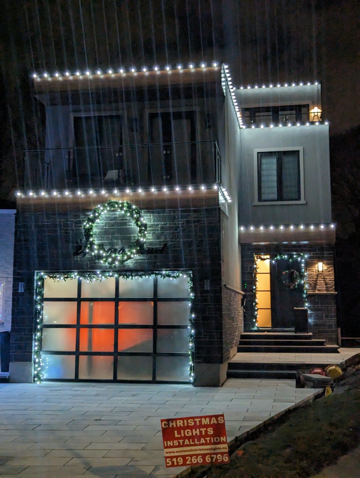 Professionally installed warm-white roofline Christmas lights on a modern two-storey home at night