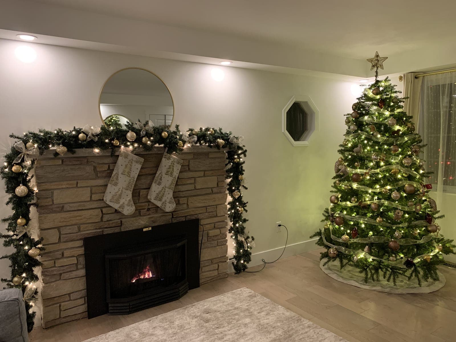 Stone fireplace with warm-white garland lights and stockings next to a decorated Christmas tree