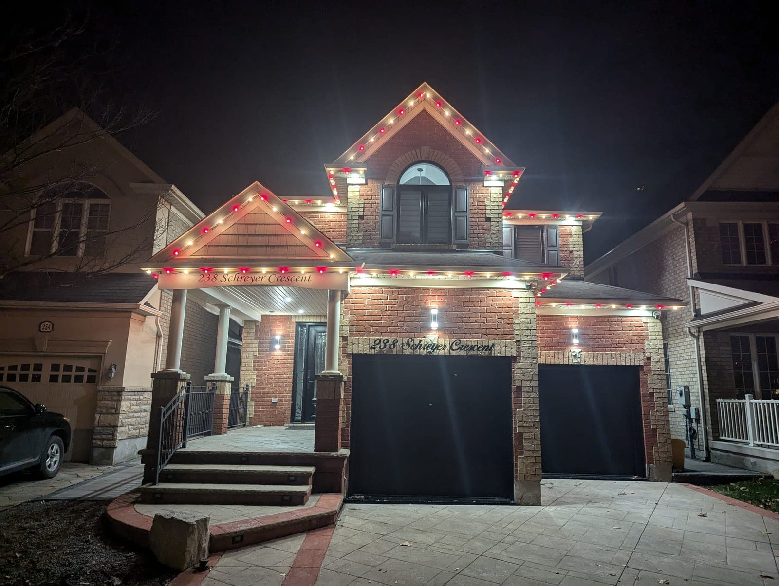 Two-storey brick home trimmed with warm-white and red C9 Christmas lights over the garage and gables