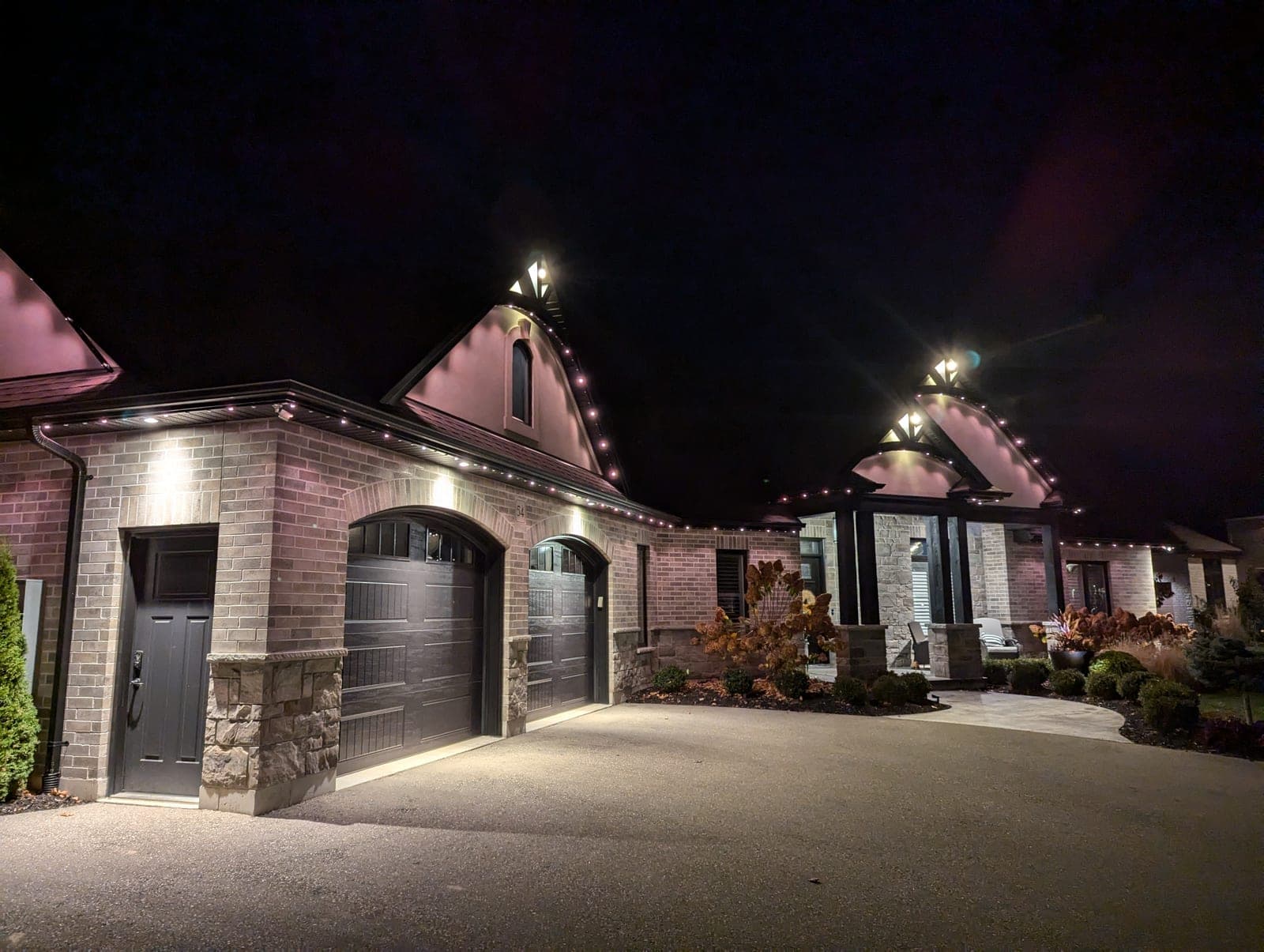 Upscale brick home lined with warm-white C9 roofline Christmas lights at night
