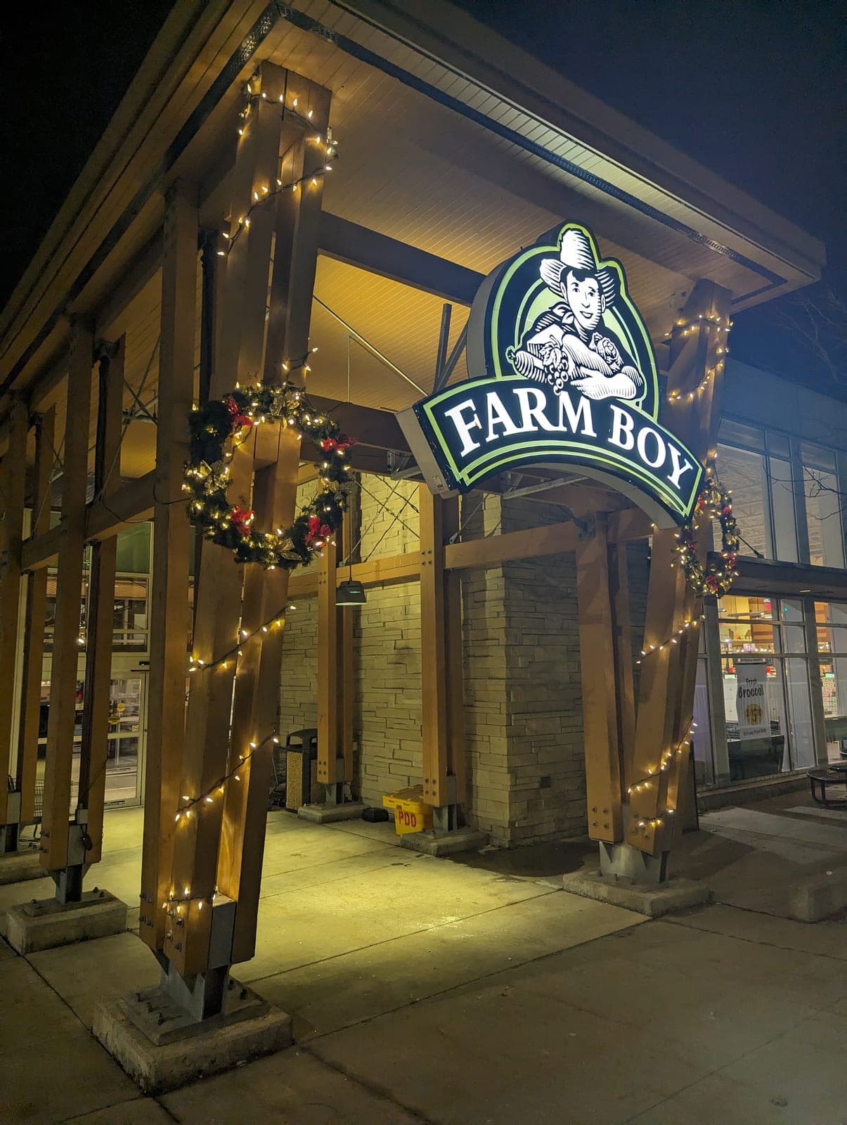 Warm-white Christmas string lights and lit wreaths on a commercial grocery storefront entrance at night
